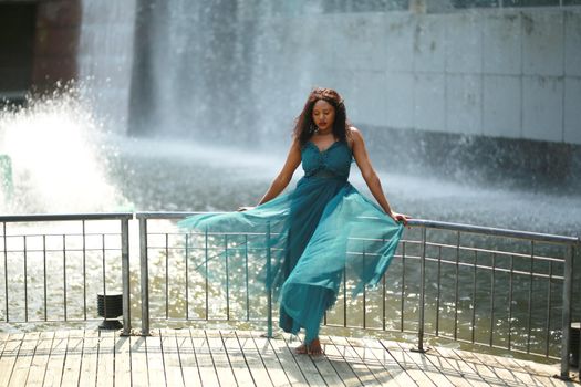 Cheerful young woman standing outdoor against water park in the garden.