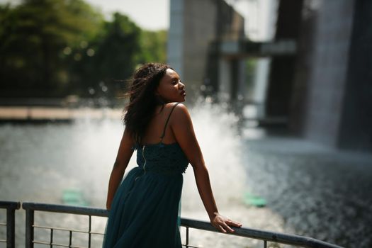 Cheerful young woman standing outdoor against water park in the garden.