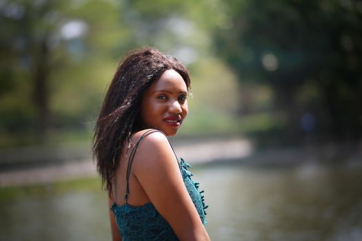 Cheerful young woman standing outdoor against water park in the garden.