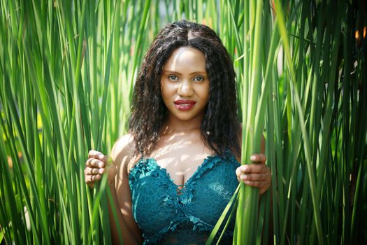 Cheerful young woman standing among tropical leaf.