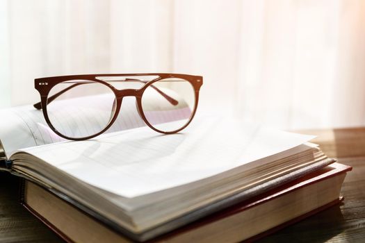 Reading glasses put on open books over wooden table beside the window