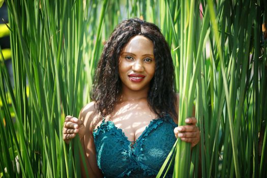 Cheerful young woman standing among tropical leaf.