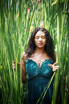 Cheerful young woman standing among tropical leaf.