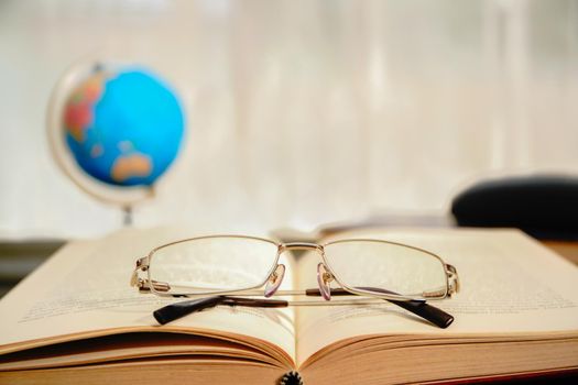 Reading glasses put on open book over wooden table