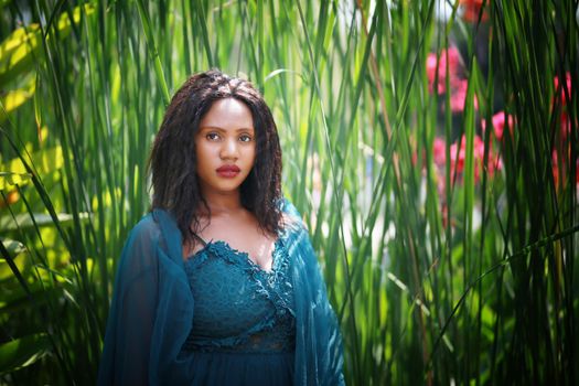 Cheerful young woman standing among tropical leaf garden.