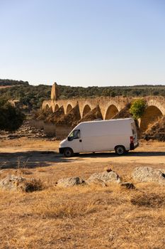 Camper van in Alentejo landscape with abandoned destroyed Ajuda bridge behind, in Portugal