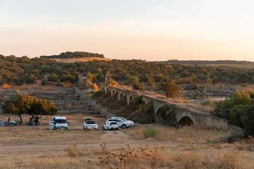 People having a picnic in Alentejo landscape with abandoned destroyed Ajuda bridge on the background at sunset, in Portugal