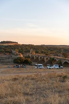 People having a picnic in Alentejo landscape with abandoned destroyed Ajuda bridge on the background at sunset, in Portugal