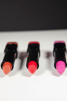 Three shades of red and pink lipsticks on a white background