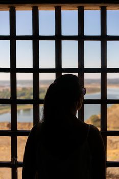 Woman in silhouette viewing of Juromenha castle with grid window in Alentejo landscape, in Portugal