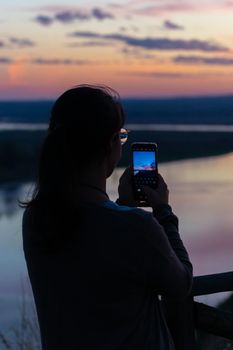 Woman photographing beautiful river landscape at sunset