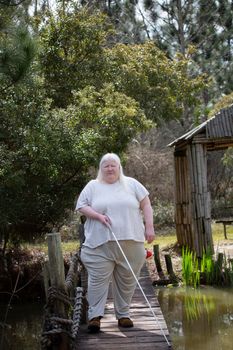 Happy blind woman on a wooden bridge over a pond with her eyes shut
