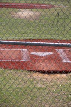 Home plate of an empty baseball field through a fence