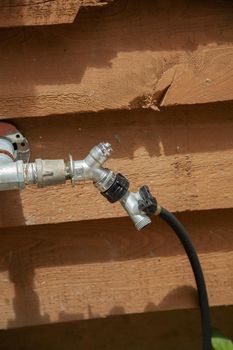 Metal outdoor water spigot near a brown planked building