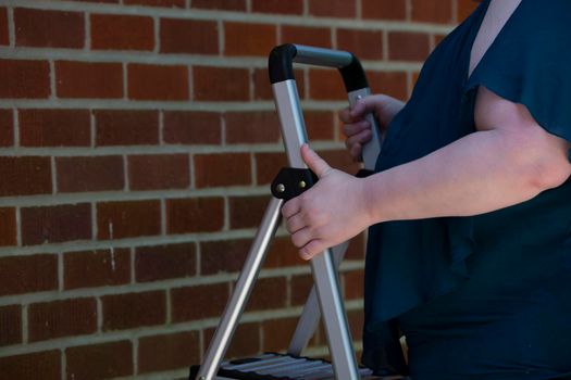 Woman setting up a step ladder near a red brick wall