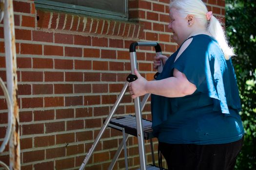 Albino woman setting up a step ladder near a red brick wall to look for necessary repairs