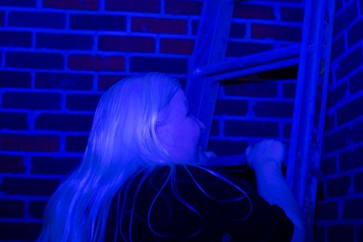 Woman climbing a ladder up a brick wall, covered in a blue hue