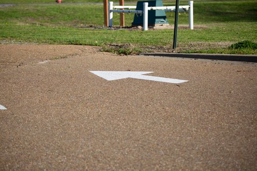 White arrow on an asphalt road, pointing away