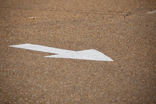 White arrow on an asphalt road, pointing toward the user