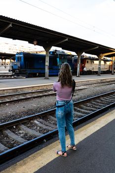 Young girl walking alone on train platform and taking photos on railway station