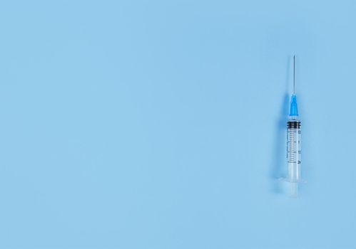 Single use syringe on a blue background. Simple flat lay with copy space.