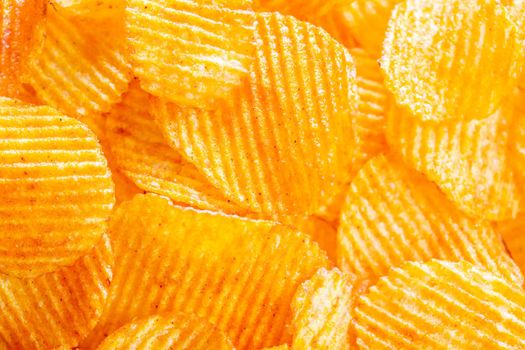 Background of yellow golden grooved fried potato chips with bright lit