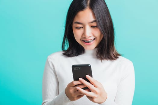 Portrait of Asian woman smile she holding and typing text message on a smartphone, female excited cheerful her reading mobile phone some social media isolated on a blue background, Technology concept