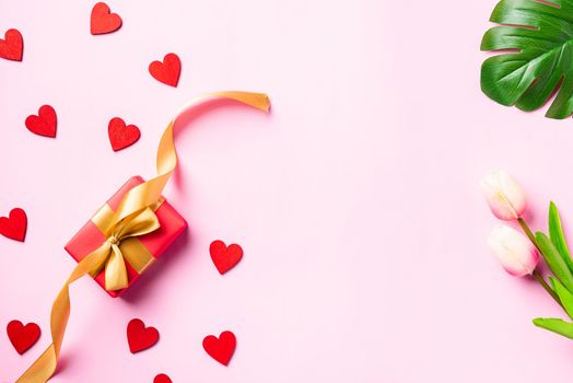 Happy Valentine's day composition background concept. Red gift box with a golden bow ribbon and wood red hearts for love isolated on pink background with copy space. Top View from above