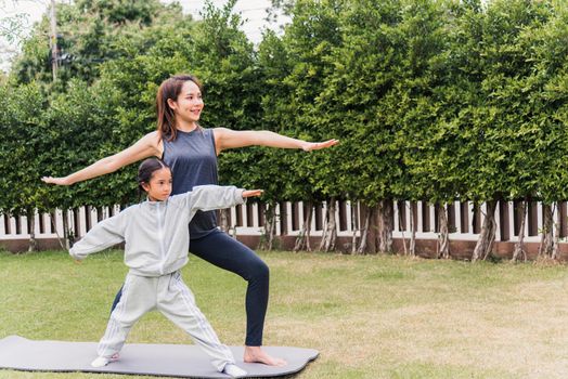 Asian young mother practicing doing yoga exercises with her daughter outdoors in meditate pose together on green grass in nature a field garden park, family sport and exercises for healthy lifestyle