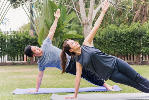 Asian couple practicing doing yoga exercises with child daughter outdoors in meditate pose together in nature a field garden park, family sport and exercises for healthy lifestyle