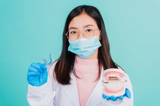 Asian beautiful woman dentist holding silicone orthodontic retainers and model teeth denture isolated on blue background, Teeth retaining tools after removable braces, Orthodontics dental healthy care