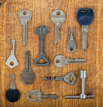 Many assorted old multi-colored metal antique vintage keys of different shapes on wooden scratched table background. Home security concept.