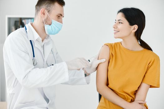 caring doctor in protective gloves to stick the injection to a woman in t-shirt with adhesive tape. High quality photo