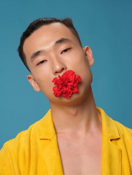 Asian man with a red flower in his teeth on a blue background. High quality photo