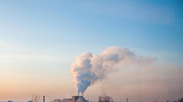 White thick smoke from the boiler room chimney. Smoke against the blue sky. Air pollution. Heating of the city. Industrial zone.