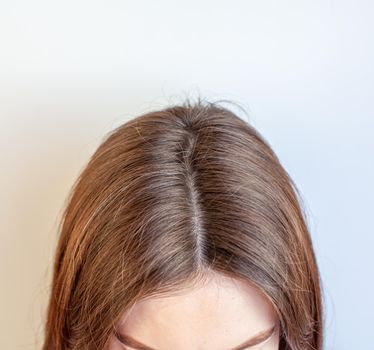 A woman's head with a parting of gray hair that has grown roots due to quarantine. Brown hair on a woman's head close-up.