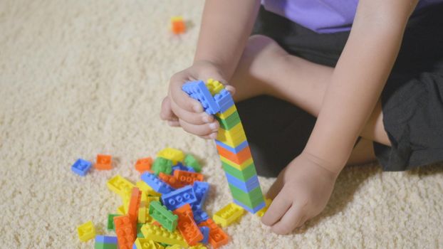 Happy Asian kid boy preschool playing creative plastic toy blocks staying at home. Funny little child sitting building tower of colorful block, Educational construction game concept