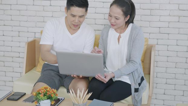 Asian family couple husband and wife work and using laptop computer analyzing finances discuss. Cheerful loving couple smile shopping order products online together from home by computer, 