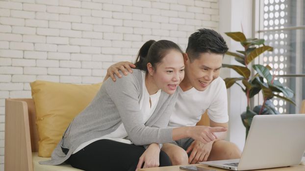 Happy Asian family couple husband and wife laughing sitting on sofa using laptop computer webcam technology talking making online social distance video call to their children at home.