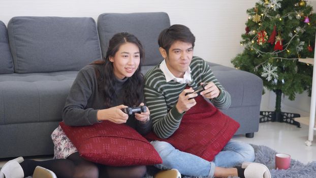 Happy Asian beautiful young family couple husband and wife smile and laugh enjoying funny with each other playing video game, holding joysticks console. Happiness and gaming concept.