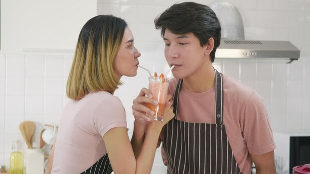 Happy Asian beautiful young family couple husband and wife enjoying arms entwined drinking fresh apple smoothie juice in kitchen on glass together in morning at home. Healthy lifestyle concept