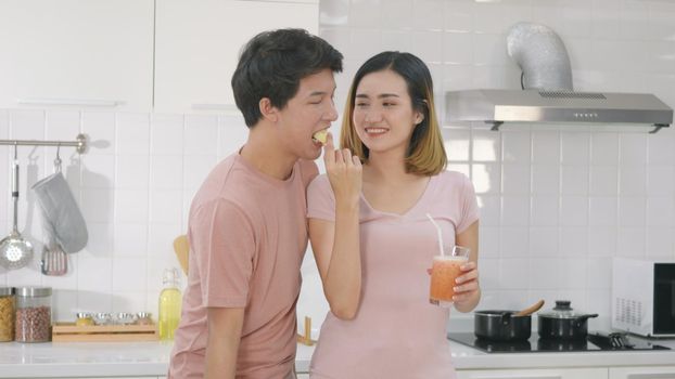 Happy Asian beautiful young family couple husband and wife enjoying drinking fresh apple smoothie juice in kitchen together at home. woman poured juice from blender for man to drink. Healthy lifestyle