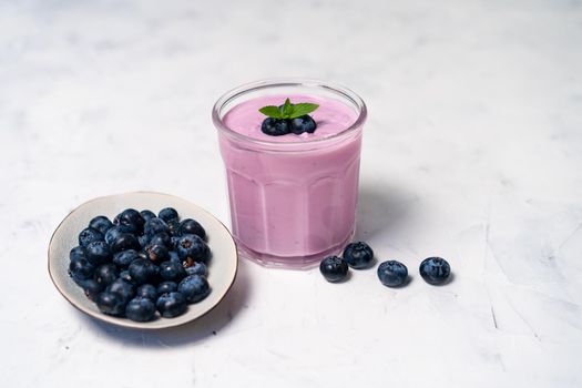 Tasty fresh blueberry yoghurt shake dessert in glass standing on white table background. Homemade berry smoothie. Healthy eating. Diet food yogurt