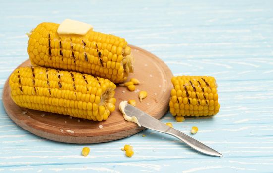 Grilled hot Corn cob lies on round cutting board plate blue wooden table background. Copy space for text.