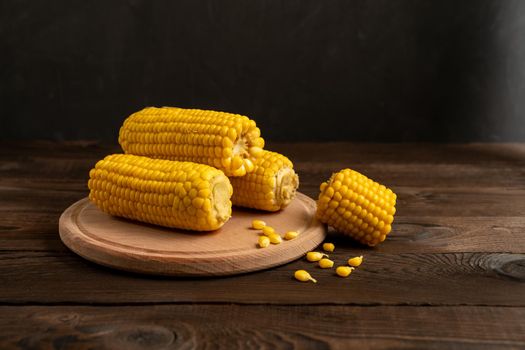 Corn cob with lies on round cutting board plate wooden table background. Copy space for text.
