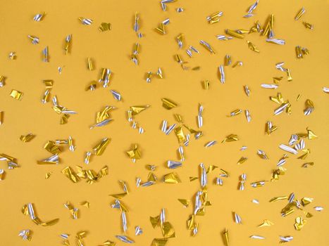 Confetti foil pieces on a yellow background. Abstract festive backdrop.