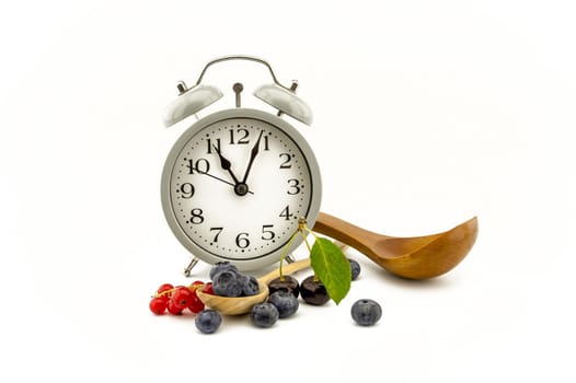 Culinary still life with old-fashioned alarm clock, wooden spoon, cherries, red currants and blueberries over white background