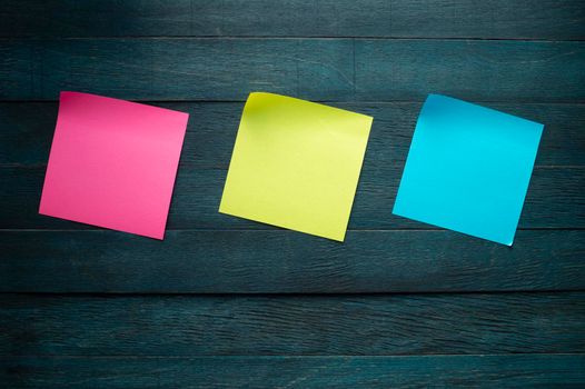Pink yellow and blue blank adhesive note stickers with curled corners on blue rustic board. Free copy space for text