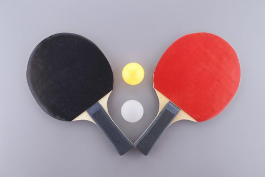 Red and black table tennis racks with a white and an yellow ping pong ball on grey background
