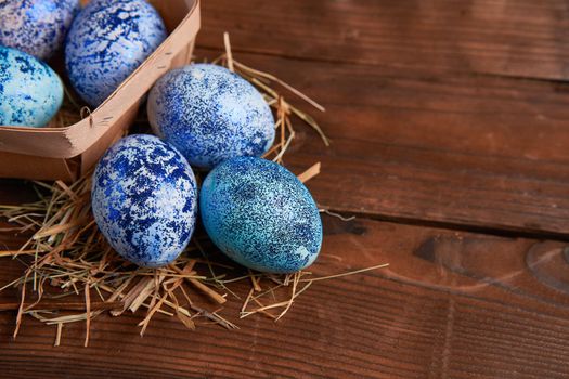 Blue chicken eggs lie in round wooden basket which stands on a dark wooden table. Easter background. Seasonal holiday flat lay with free space for text. Classic blue color of the year 2020